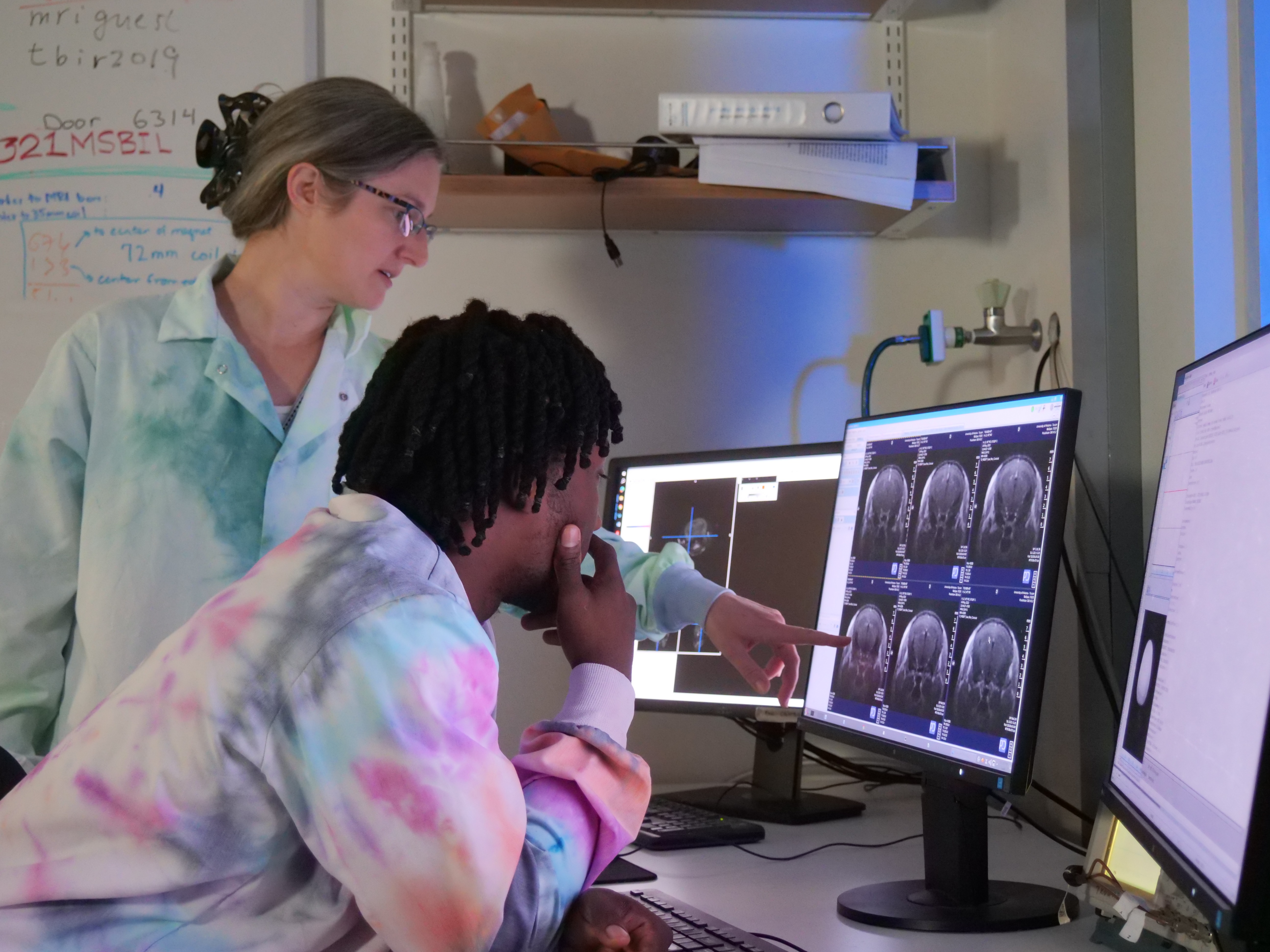 Woman points at a screen with brain scans while a young man looks on curiously
