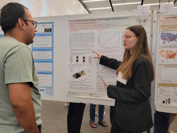 Student explains their research poster to a man in a green shirt