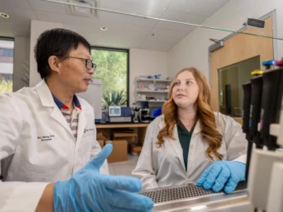 Two people discuss in a lab wearing white coats and blue latex gloves