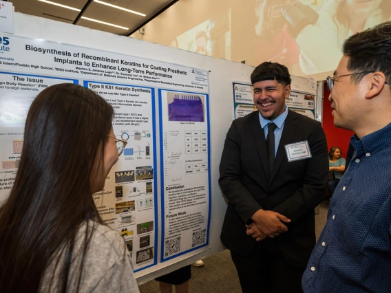 Three individuals engaged in a discussion at a scientific poster presentation about "Biosynthesis of Recombinant Keratin for Coating Implants" at the BIO5 Institute's KEYS Research Internship Showcase.