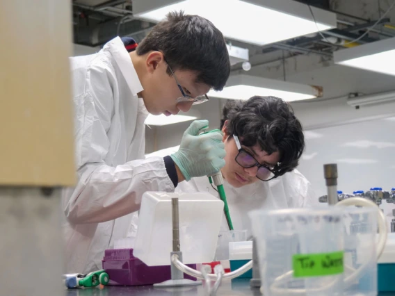 Two individuals in lab coats conducting an experiment in a laboratory setting, using pipettes and other scientific equipment.