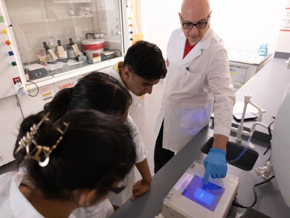Three individuals in lab coats observing a scientific experiment involving a glowing blue light in a laboratory setting.
