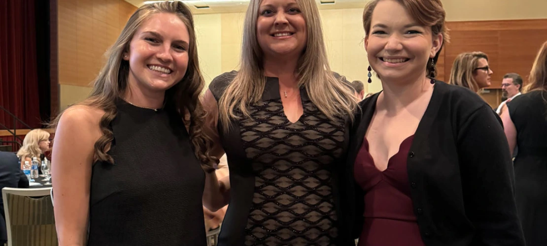 Three individuals smiling at a formal event, dressed in elegant attire.