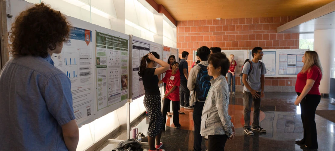People viewing and presenting research posters in a university hallway.