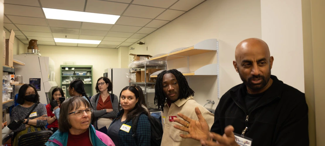Group of people with name tags listening to a speaker in a laboratory.