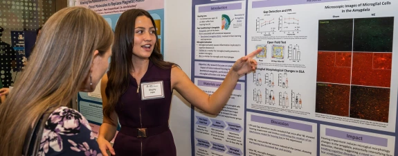 Two individuals at a science conference discussing a research poster about neurological studies, with one person pointing at a chart on the poster.