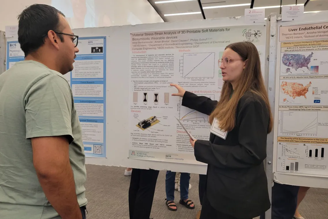 Student explains their research poster to a man in a green shirt