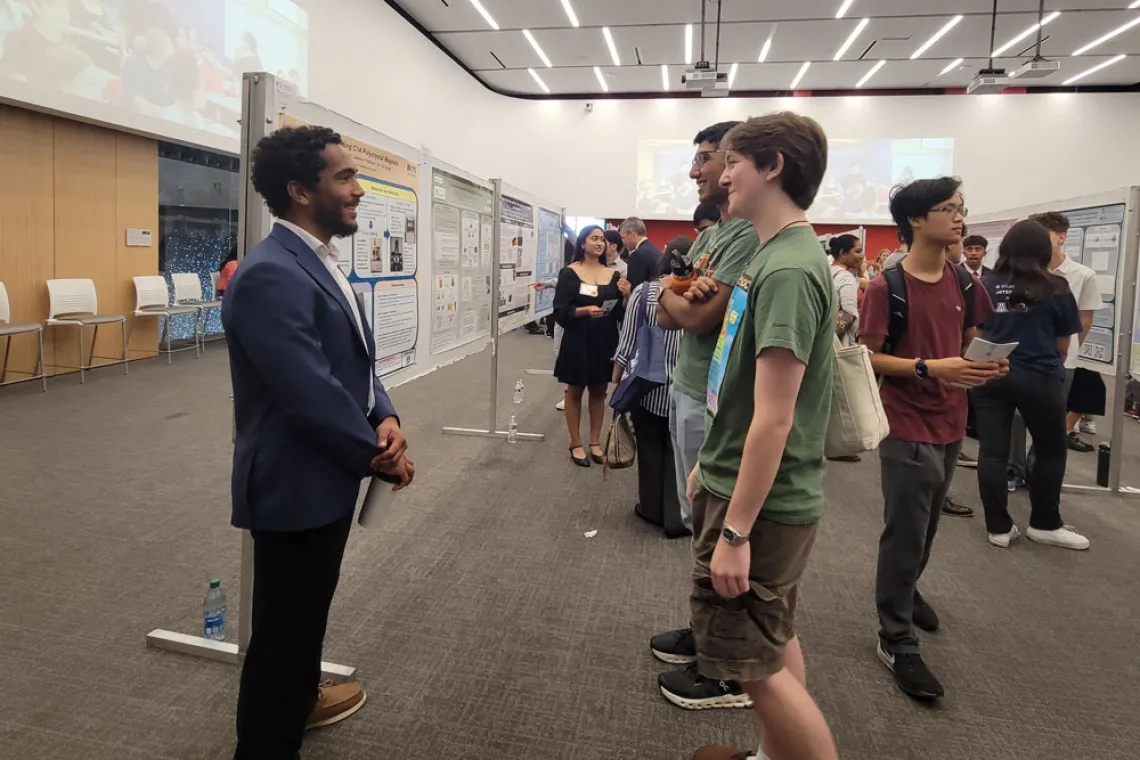 Student explains his research in front of his poster