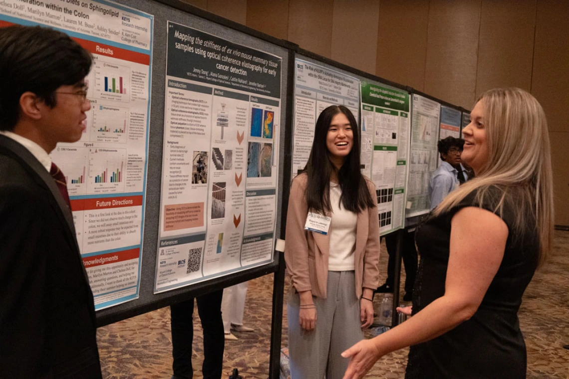 Three individuals standing by research posters, engaging in a discussion at a professional conference.