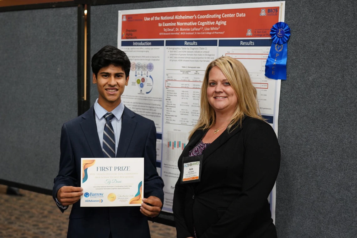 Young person stands with a certificate in front of a scientific poster