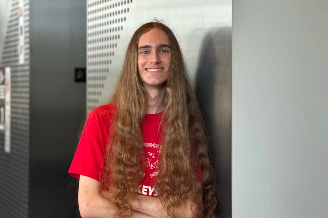 Person with long brown hair wearing a red KEYS tshirt smiles confidently 