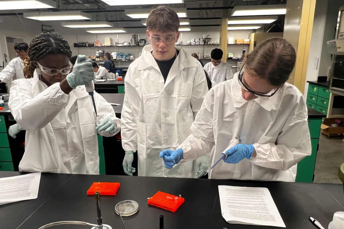 Three young people in white lab coats and protective gear work in a laboratory setting