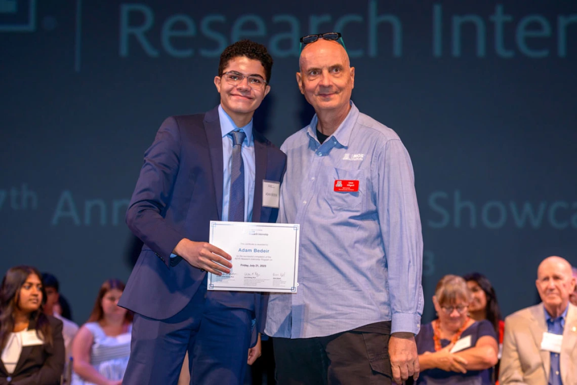 Two people shaking hands on stage at a Research Internship Showcase event, with one person handing a certificate to the other.