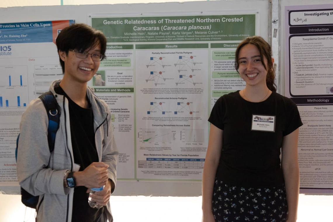 Two individuals standing in front of scientific posters at a conference, smiling. The poster discuss genetic research on Northern Crested Caracaras.