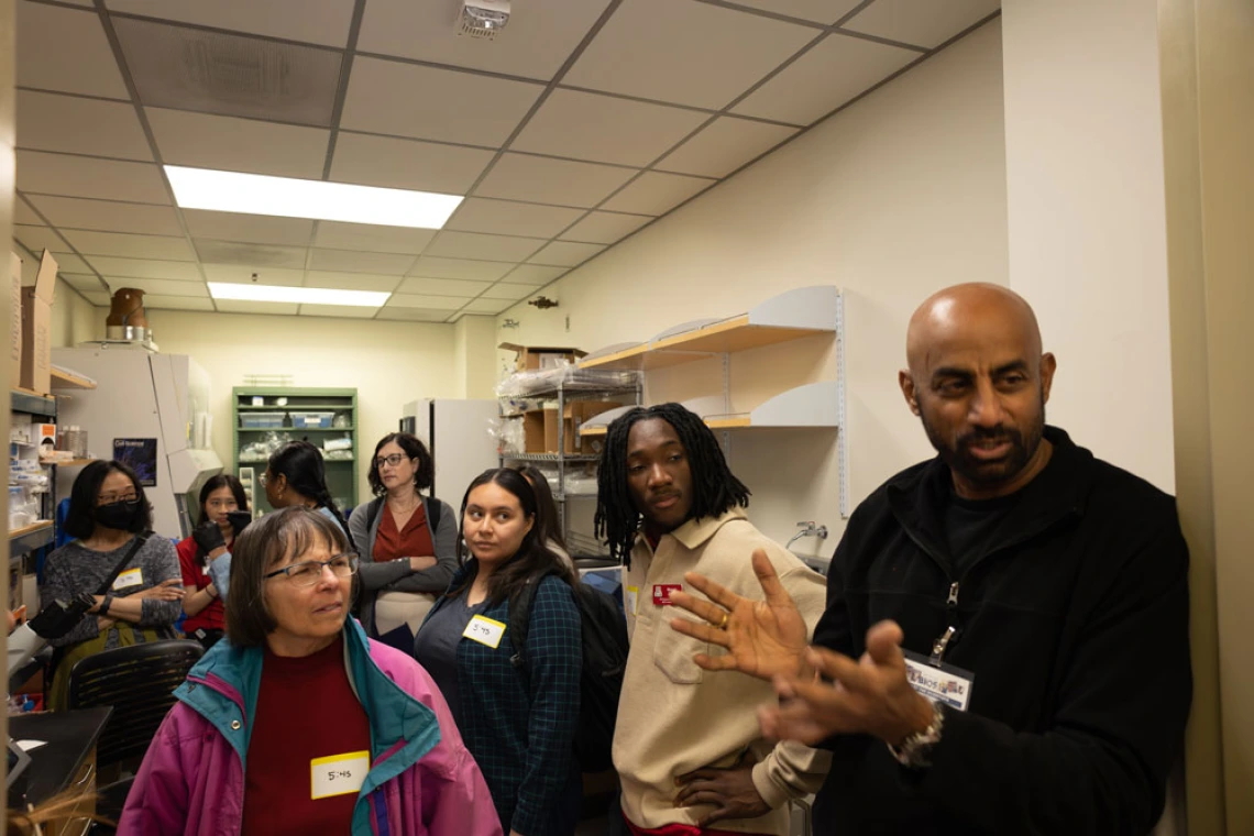 Group of people with name tags listening to a speaker in a laboratory.