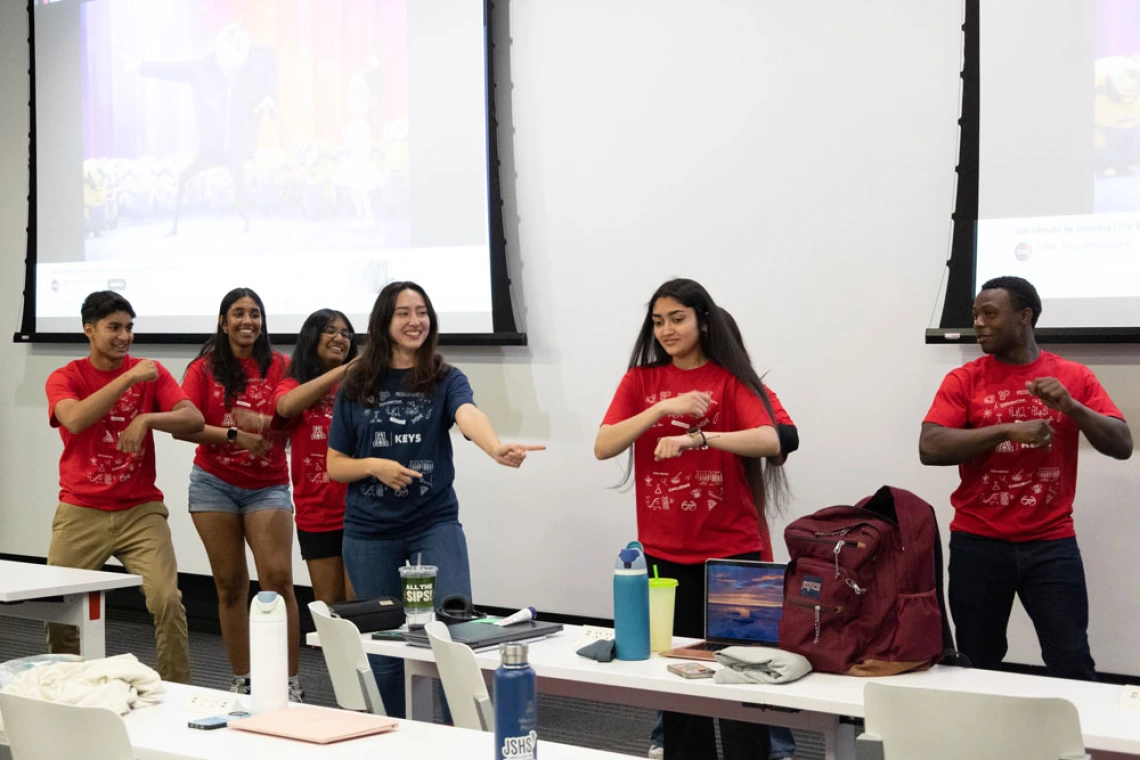 Group of students in KEYS red and blue shirts doing a team-building activity in a classroom, with a presentation screen visible in the background.
