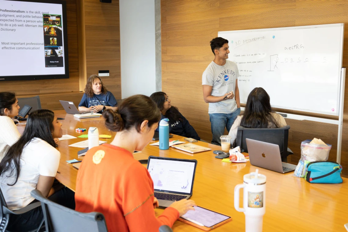 Person presenting a flowchart on a whiteboard during a workshop at a well-lit conference room filled with participants using laptops.