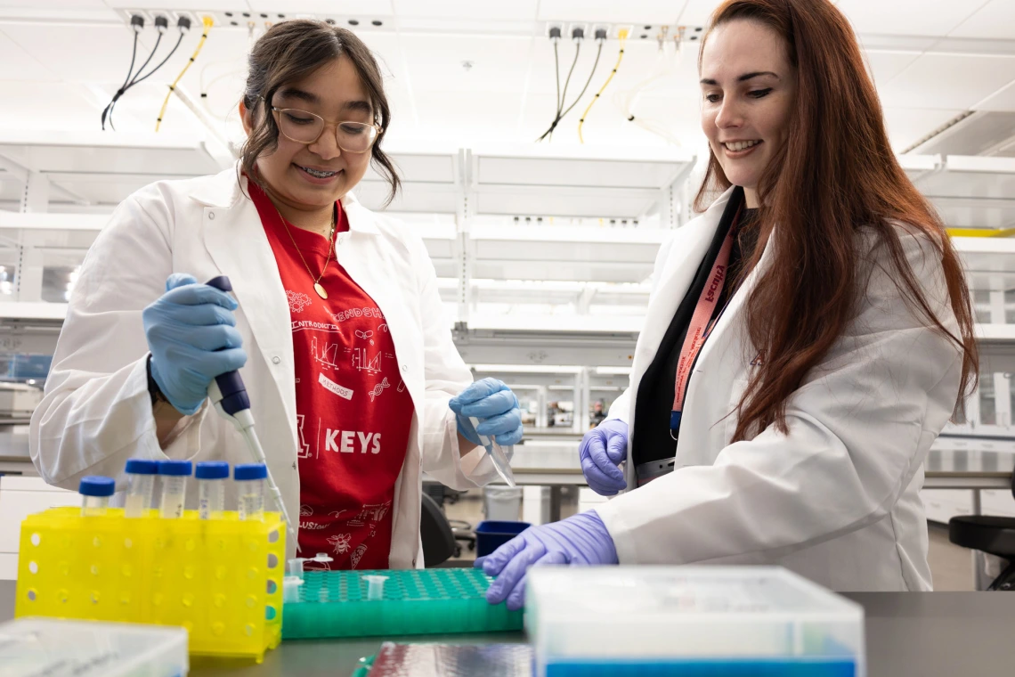 Two people pipetting samples into a tray in a modern lab.