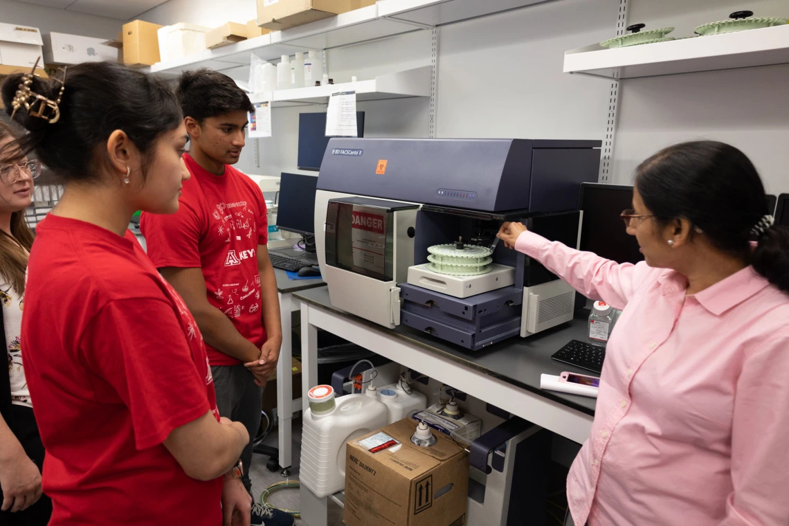 Group of students observing a teacher demonstrating equipment in a laboratory setting.