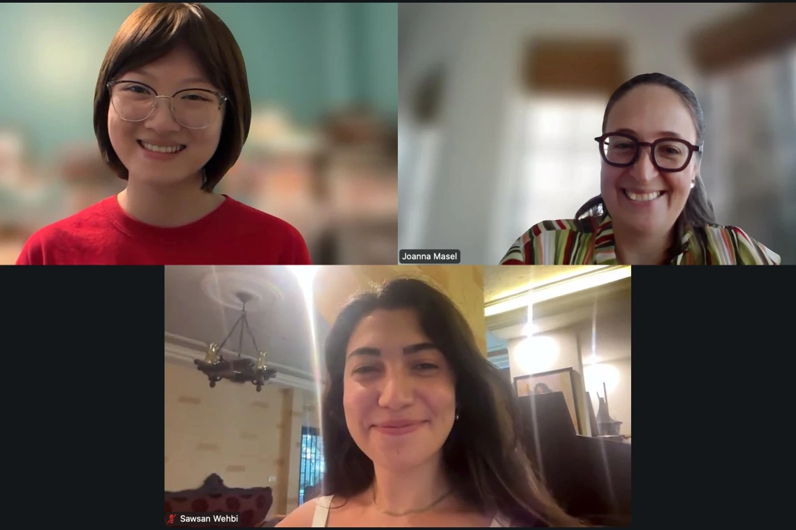 A screenshot of a video call featuring three individuals smiling. The top row shows one person in a red shirt and person in a patterned shirt with the name Joanna Masel on the right. The bottom row is a smiling person with the name Sawsan Wehbi.