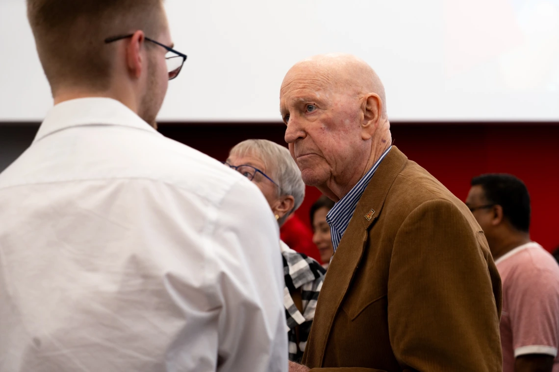 An older adult is engaged in a conversation with a younger adult in a social gathering.