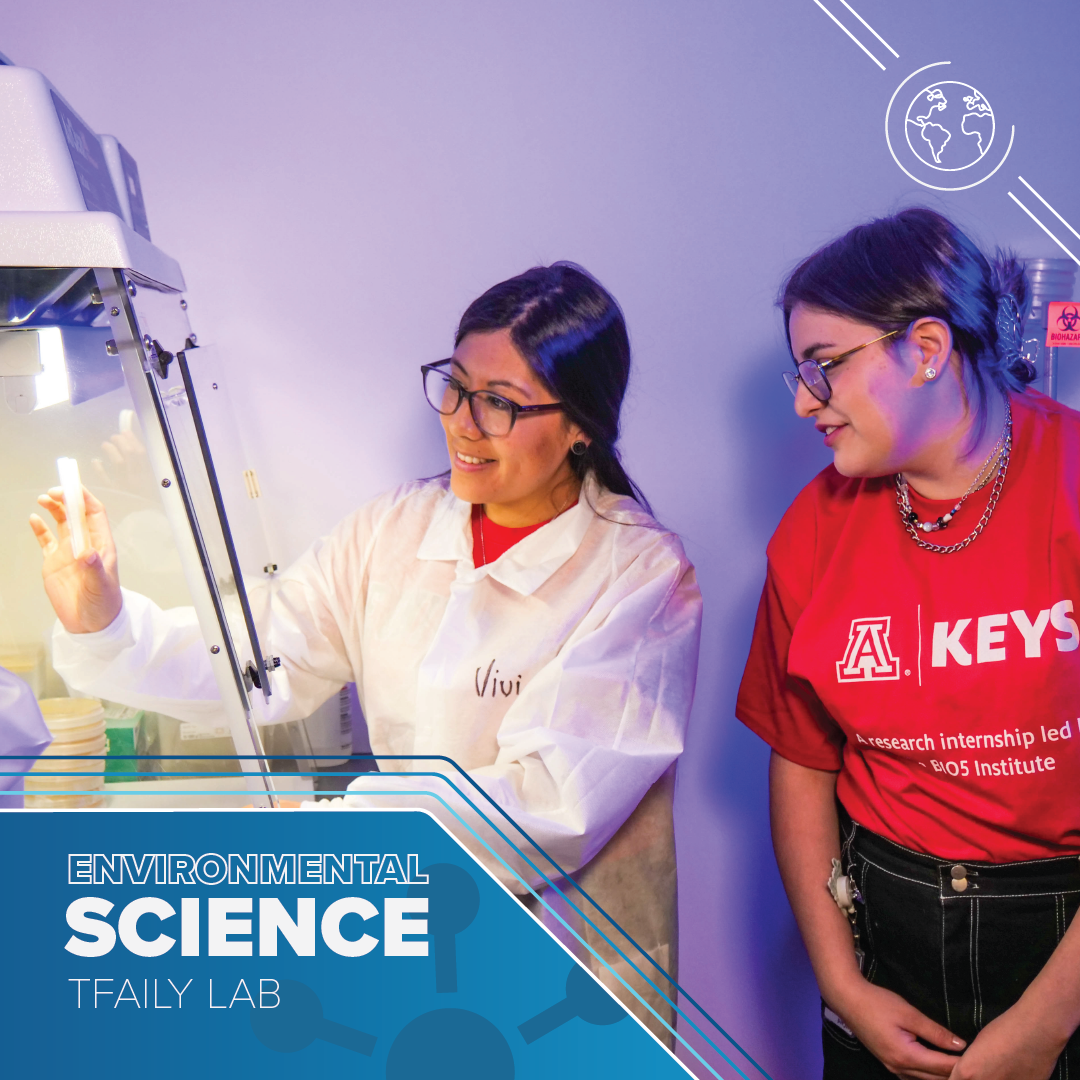 Woman with long dark hair wearing a lab coat holds up a vial in a fume hood. A young person wearing a red t-shirt with the KEYS logo looks on curiously. Text reads: Environmental Science Tfaily Lab