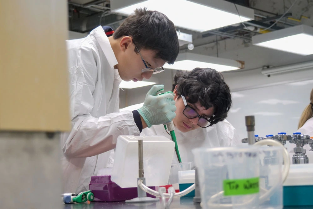 Two individuals in lab coats conducting an experiment in a laboratory setting, using pipettes and other scientific equipment.