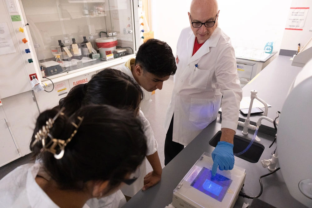 Three individuals in lab coats observing a scientific experiment involving a glowing blue light in a laboratory setting.