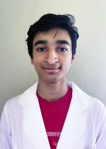 Person wearing a white lab coat over a red "Friends" T-shirt, smiling slightly against a light background.