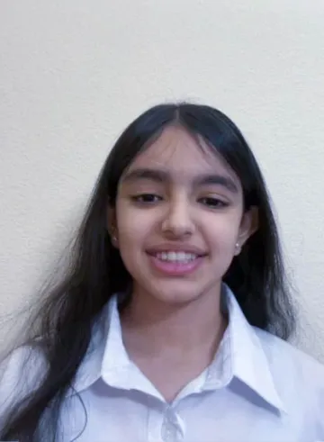 Portrait of a smiling young person wearing a white shirt, standing against a light-colored wall.