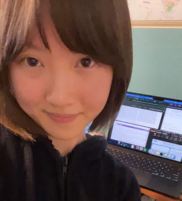 Person smiling at the camera in front of a laptop with documents on the screen.