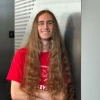 Person with long brown hair wearing a red KEYS tshirt smiles confidently 