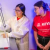 Person in white lab coat explains research to student in red KEYS t-shirt